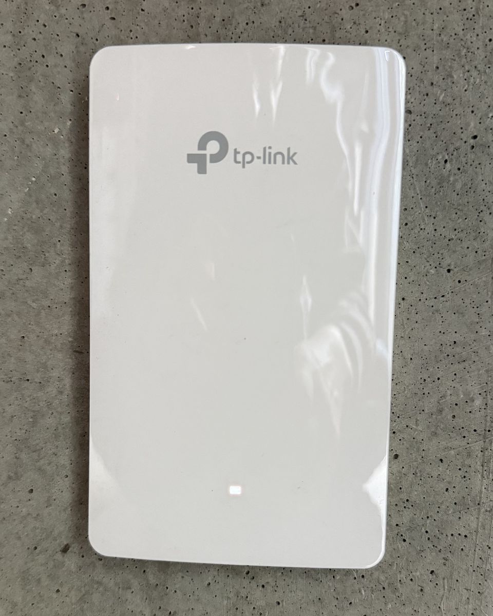 Biały punkt dostępowy Wi-Fi zamontowany na betonowej ścianie pokoju, jeszcze w folii ochronnej.