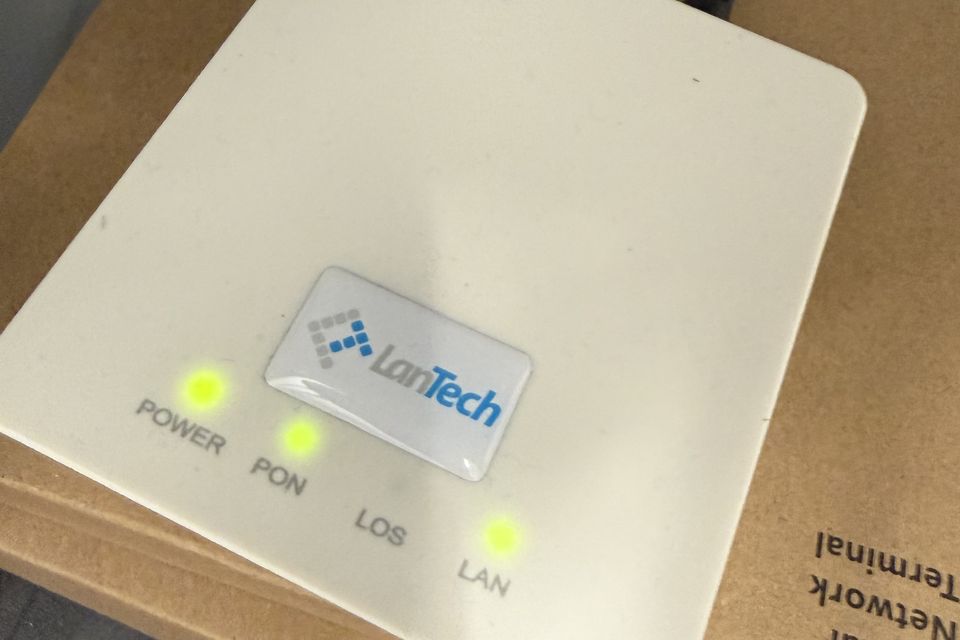 Zakończenie łącza światłowodowego z naklejką LanTech na obudowie, ze świecącymi diodami POWER, PON i LAN.