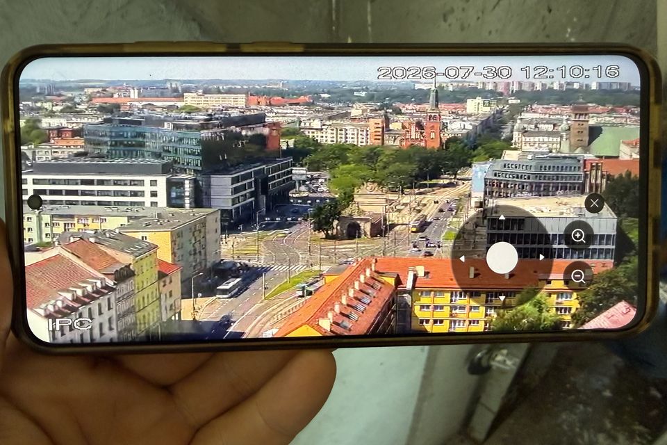 Telefon w dłoni technika z obrazem z nowej kamery na żywo: panorama Szczecina z góry i przyciski sterowania kadrem.