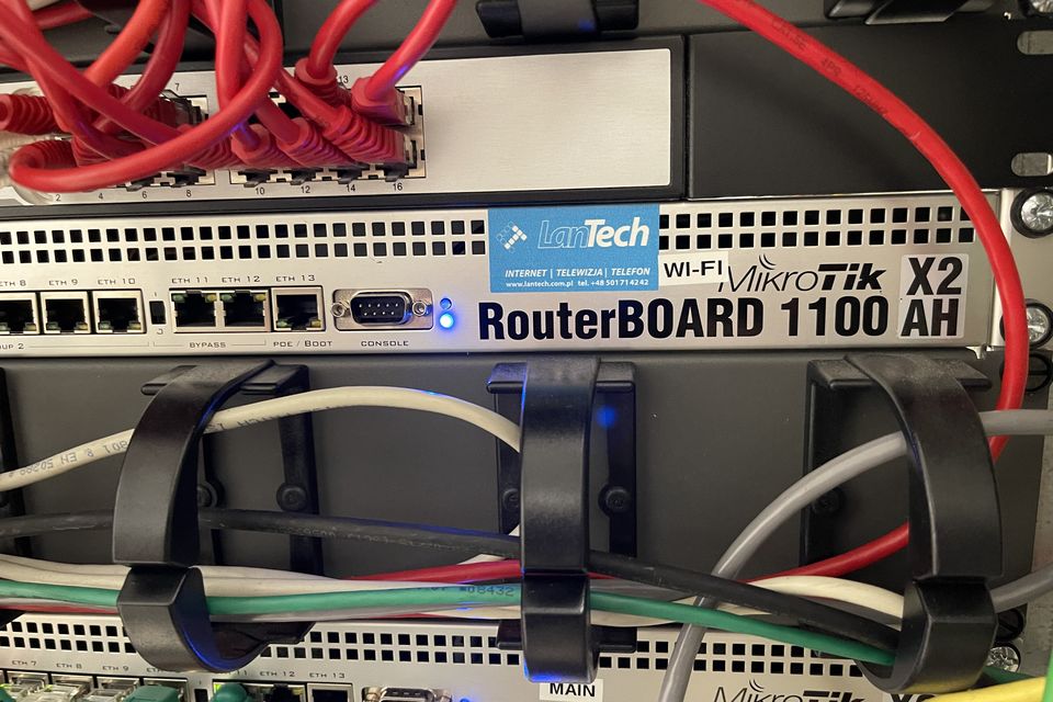 Router brzegowy w szafie z naklejką LanTech i wiązkami przewodów ujętymi w uchwyty.