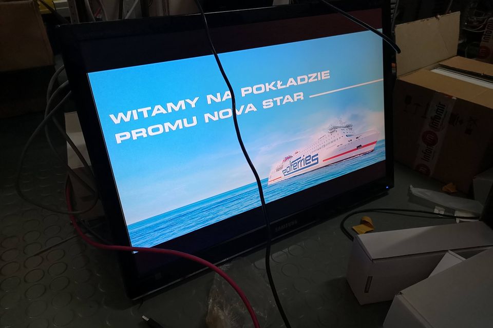 Telewizor zamontowany na pokładzie wyświetla planszę powitalną dla pasażerów.