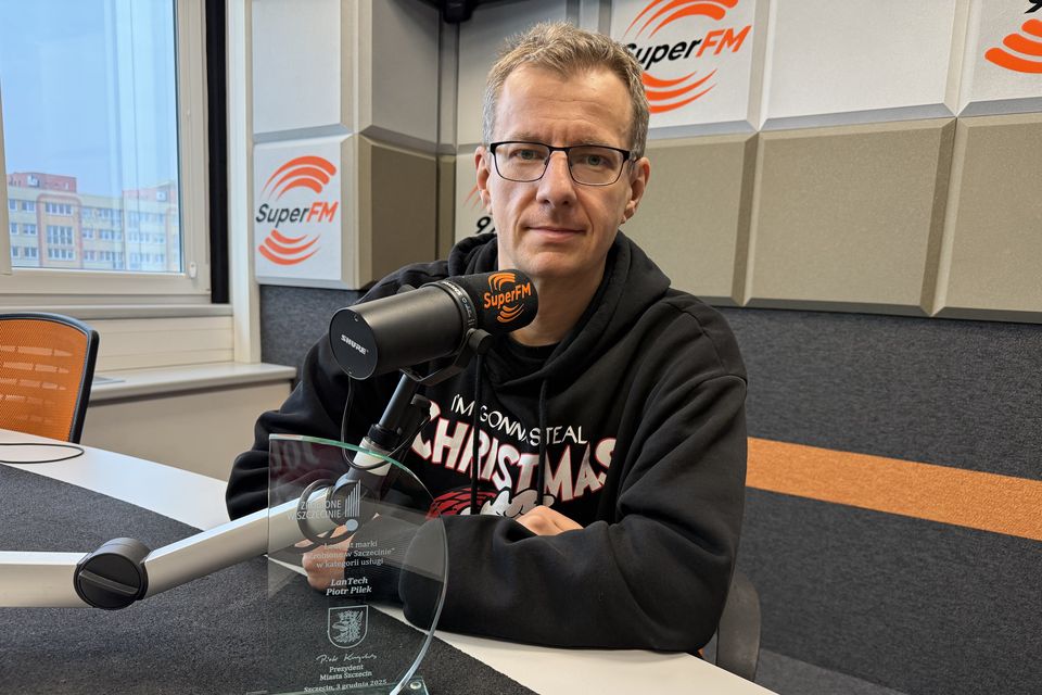 Właściciel firmy przy mikrofonie w studiu radiowym, przed nim na stole szklana statuetka.