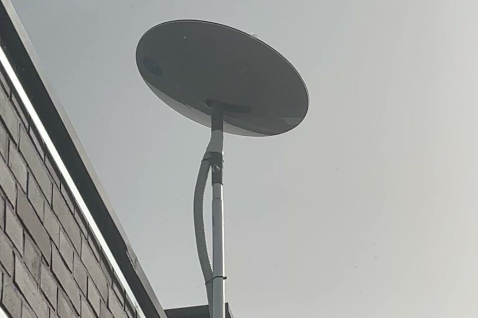 Antena internetu satelitarnego na stalowym maszcie przymocowanym do ściany budynku, kabel poprowadzony w osłonie wzdłuż masztu.