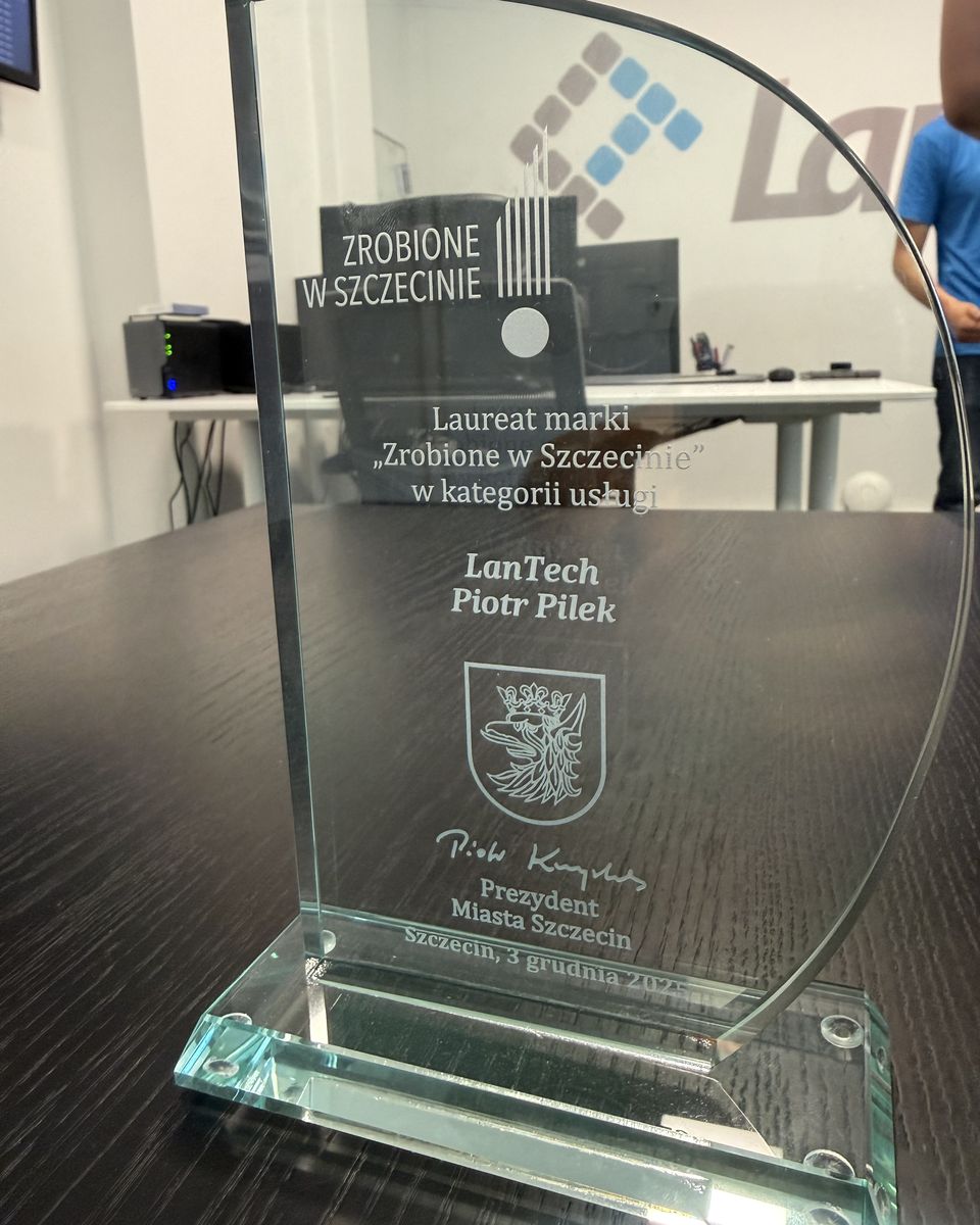 Szklana statuetka „Zrobione w Szczecinie” z grawerem LanTech Piotr Pilek na stole w biurze, za nią logo LanTech na ścianie.