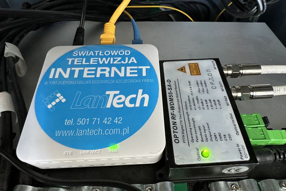 Zakończenie łącza z naklejką „Światłowód, Telewizja, Internet” obok odbiornika optycznego sygnału telewizyjnego.